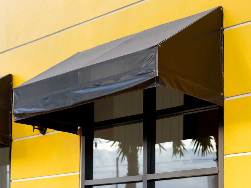 A black awning over a window on a yellow building.